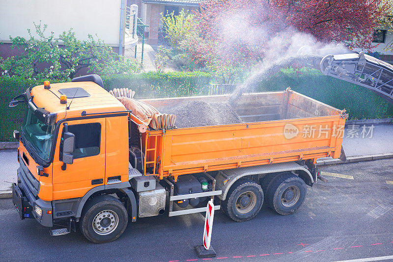 Cold milling machine removing asphalt pavement and loading it into the dump tuck. High angle view.